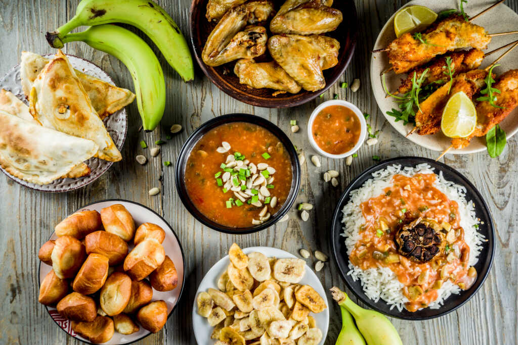 West african food concept. Traditional Wset African dishes assortment – peanut soup, jollof rice, grilled chicken wings, dry fried bananas plantains, nigerian chicken kebabs, meat pies, top view
